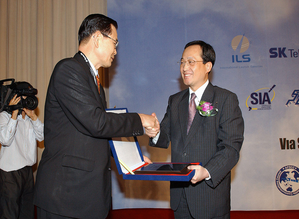 Shin Bae Kim, president of SK Telecom, is shown receiving `Asia Meritorious Award of the Year for Satellite Service` given by the APSCC.